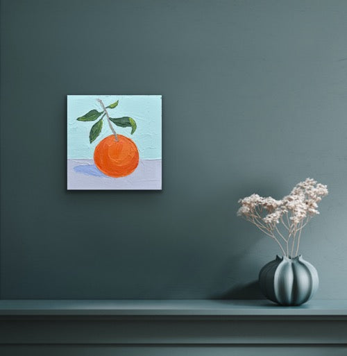 Painting of an orange on a teal wall above a shelf with a vase and flowers.