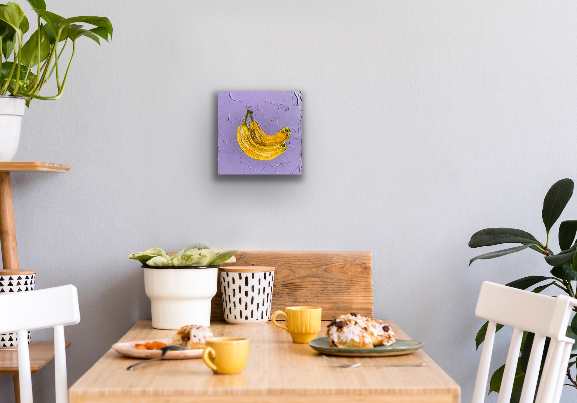Dining area with a table set for breakfast, plants, and a wall art piece.