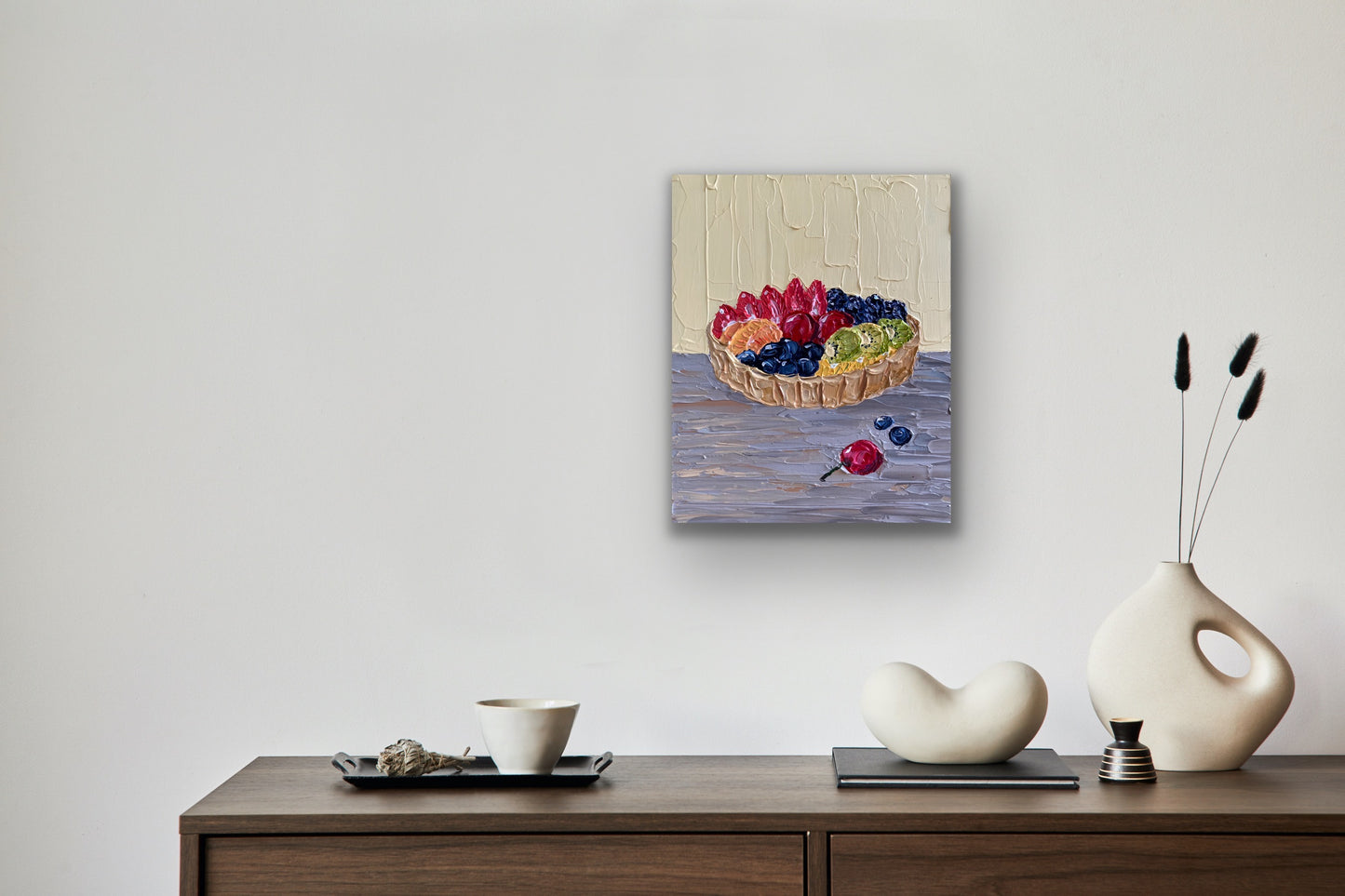 Framed artwork of a fruit basket on a wall above a wooden console table with decorative items.