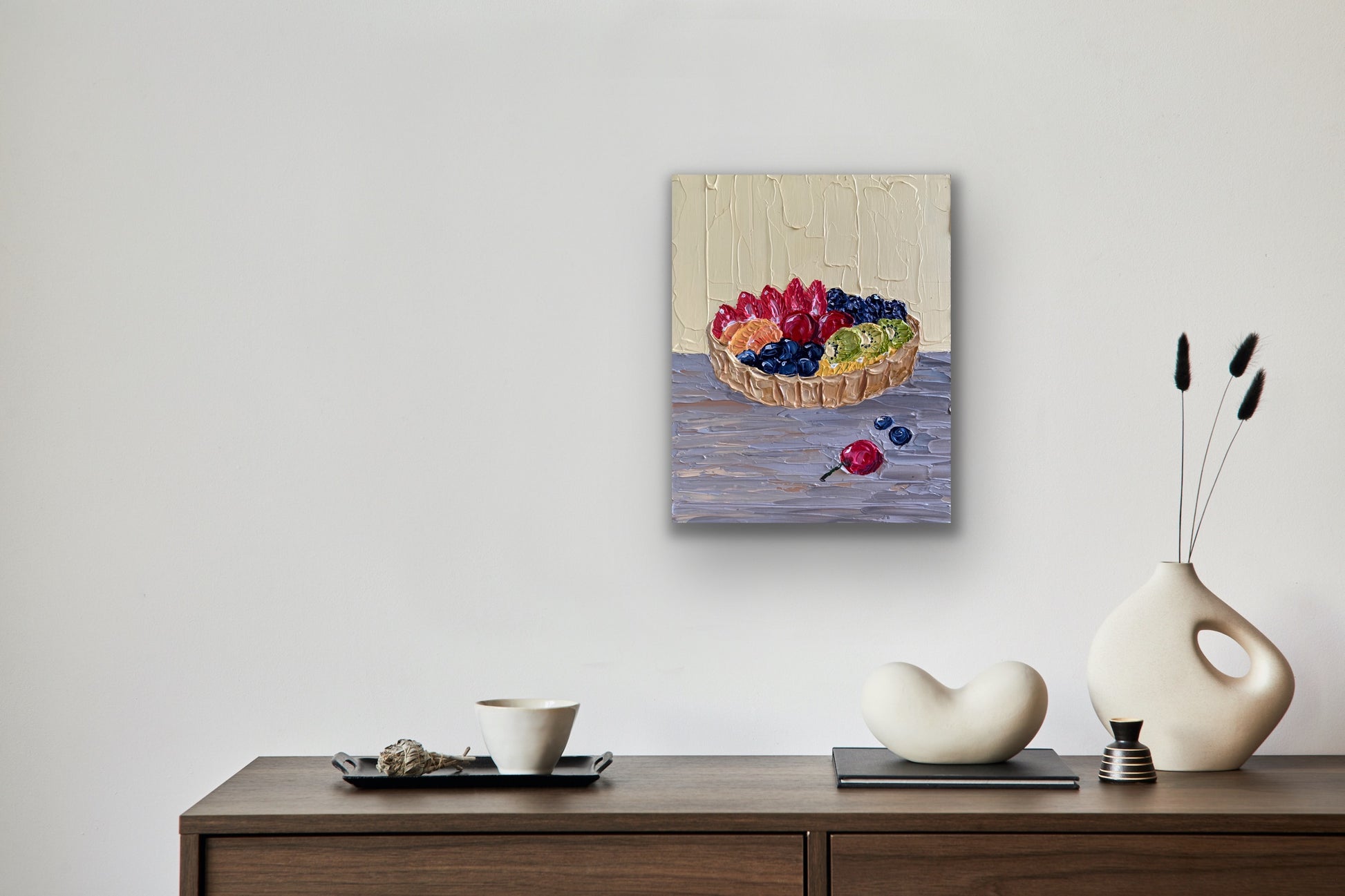 Framed artwork of a fruit basket on a wall above a wooden console table with decorative items.