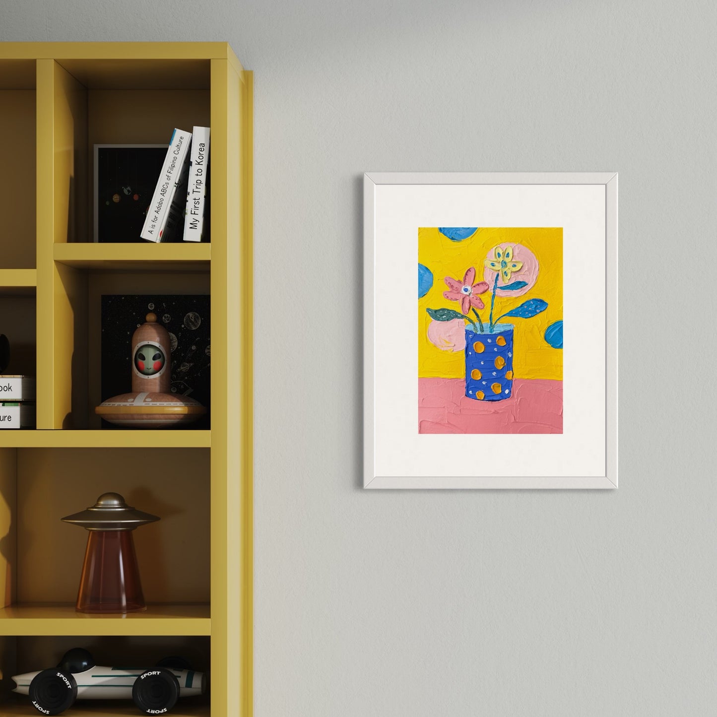 Framed artwork of a colorful flower vase on a yellow background, displayed on a gray wall next to a yellow bookshelf.