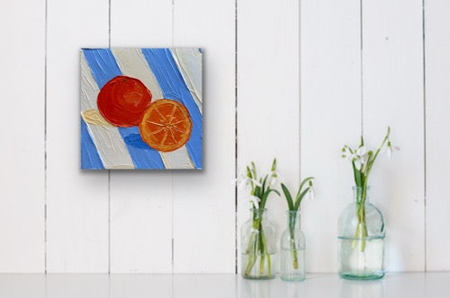 Canvas painting of oranges on a blue and white striped background, displayed on a white wall with three glass bottles containing plants below.