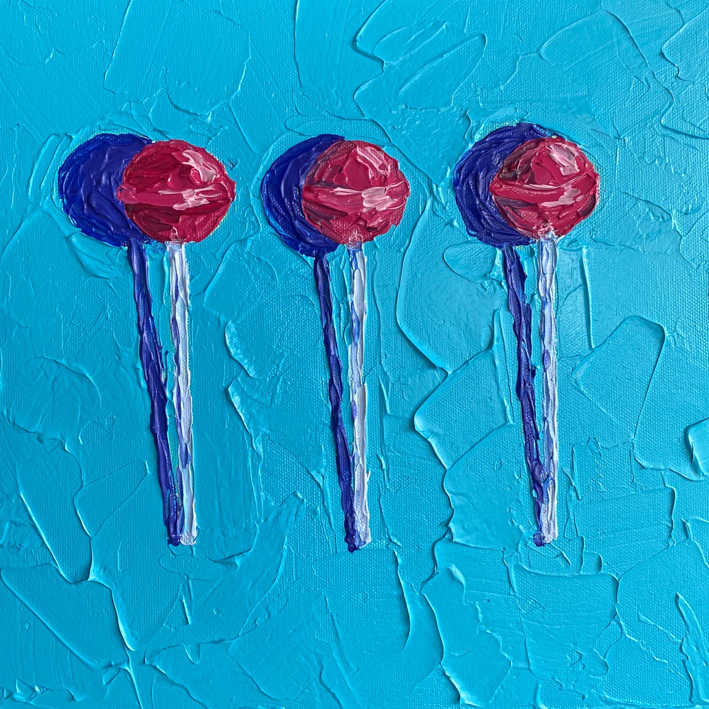 Three red lollipops on blue sticks against a textured blue background