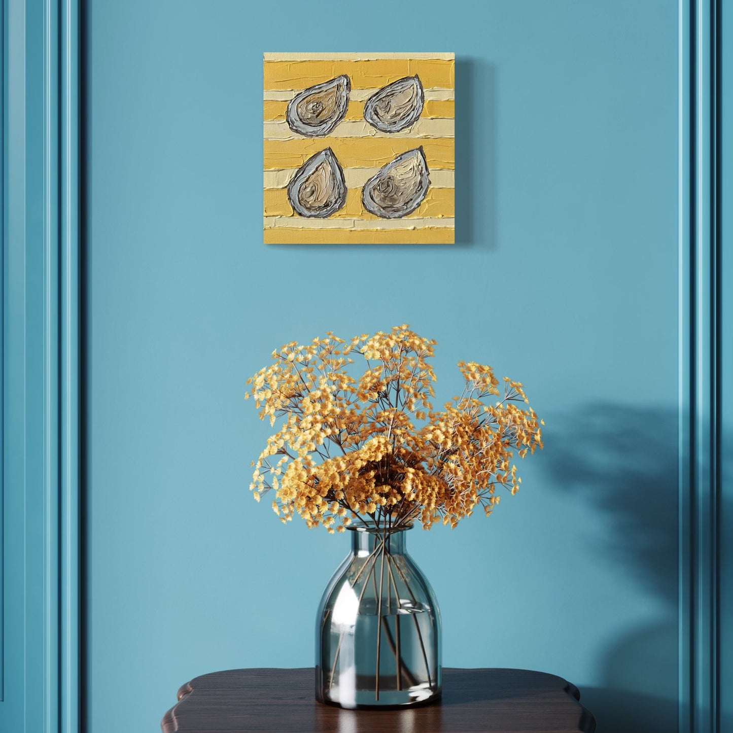 Decorative painting of oyster shells on a yellow background above a vase with dried flowers on a blue wall.