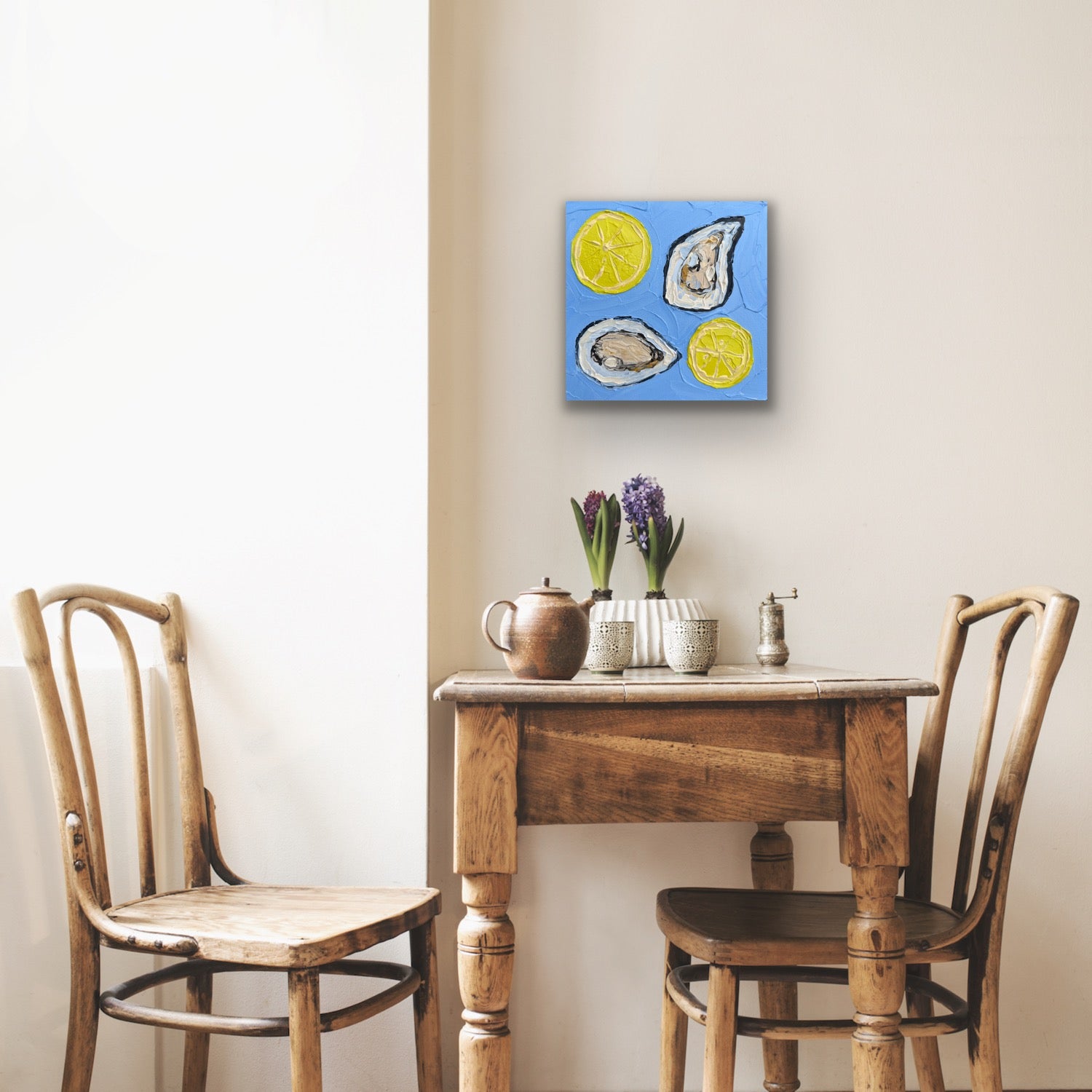 Small wooden table with two chairs and a decorative painting above it on a beige wall.